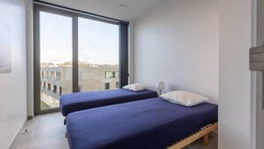 Ein modernes Schlafzimmer mit zwei Einzelbetten, einem großen Fenster und Blick auf eine Stadtlandschaft.