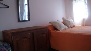 A bedroom with a wooden dresser, an orange bed with two pillows, a mirror, and a window with curtains. - Little Sunny Loft (Buenos Aires)