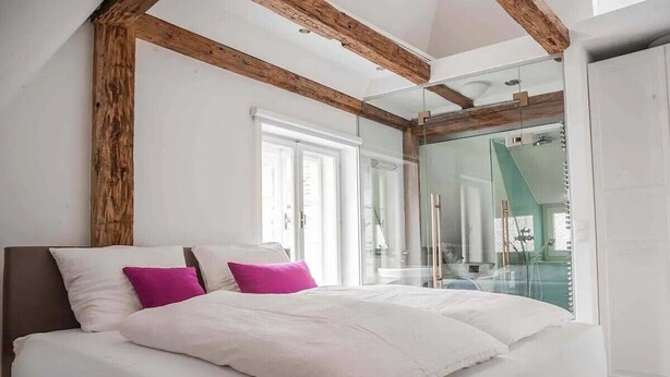 Un dormitorio moderno con una cama grande, vigas de madera y una cabina de ducha de vidrio.