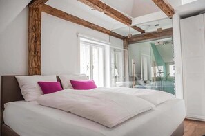 A modern bedroom with a large bed, wooden beams, and a glass shower enclosure.