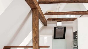 Una cocina moderna con armarios blancos, techo de vigas de madera y televisor empotrado.