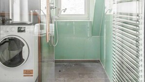 Un baño pequeño con lavadora, ducha e inodoro con cerramiento de vidrio.