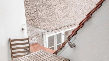 Taula i cadires de fusta en un balcó amb una paret amb relleu i una finestra.