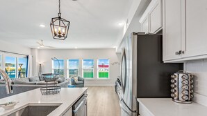 A modern kitchen with a central island, stainless steel appliances, and a view of the city through large windows. - Beachfront Condo • Rooftop Pool • Sleeps 8 (Mexico Beach)