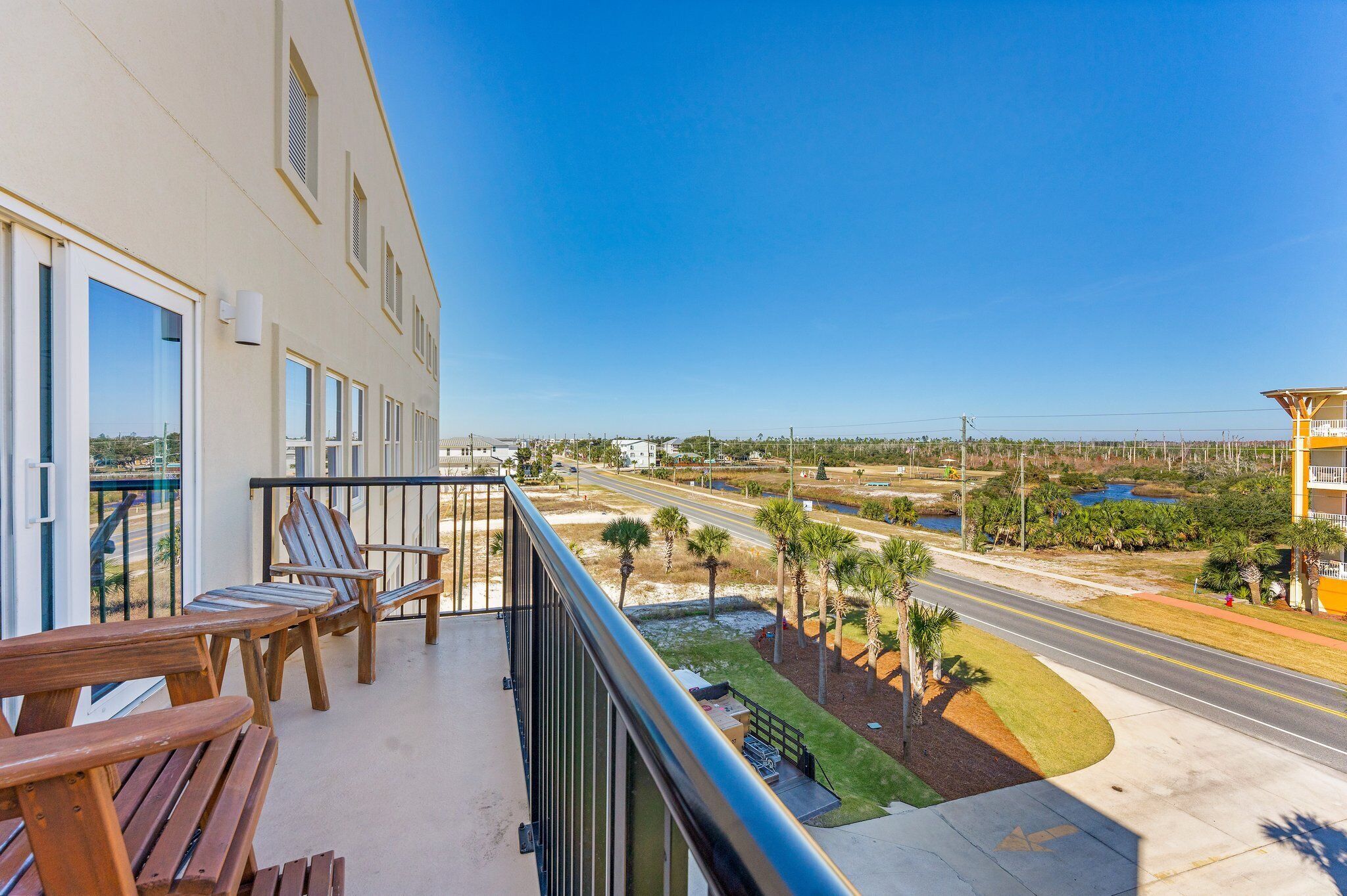 A balcony with wooden chairs and a view of a road and greenery.
