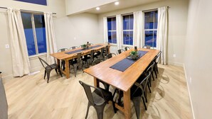 Un comedor amplio con una larga mesa de madera, varias sillas y ventanas grandes con cortinas.