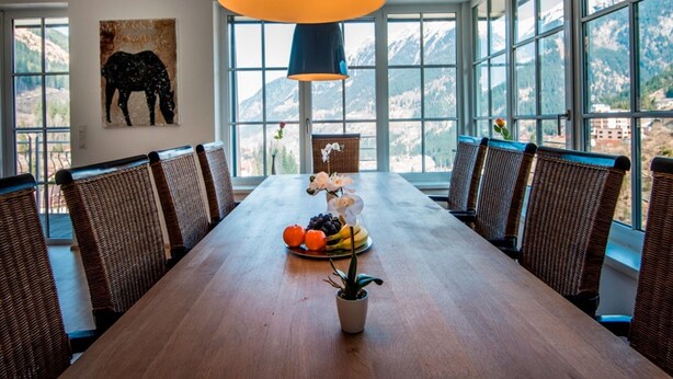 A dining area with a long wooden table, wicker chairs, a potted plant, and a fruit plate. - Penthouse in Bad Gastein Near Ski Lifts (Bad Gastein)