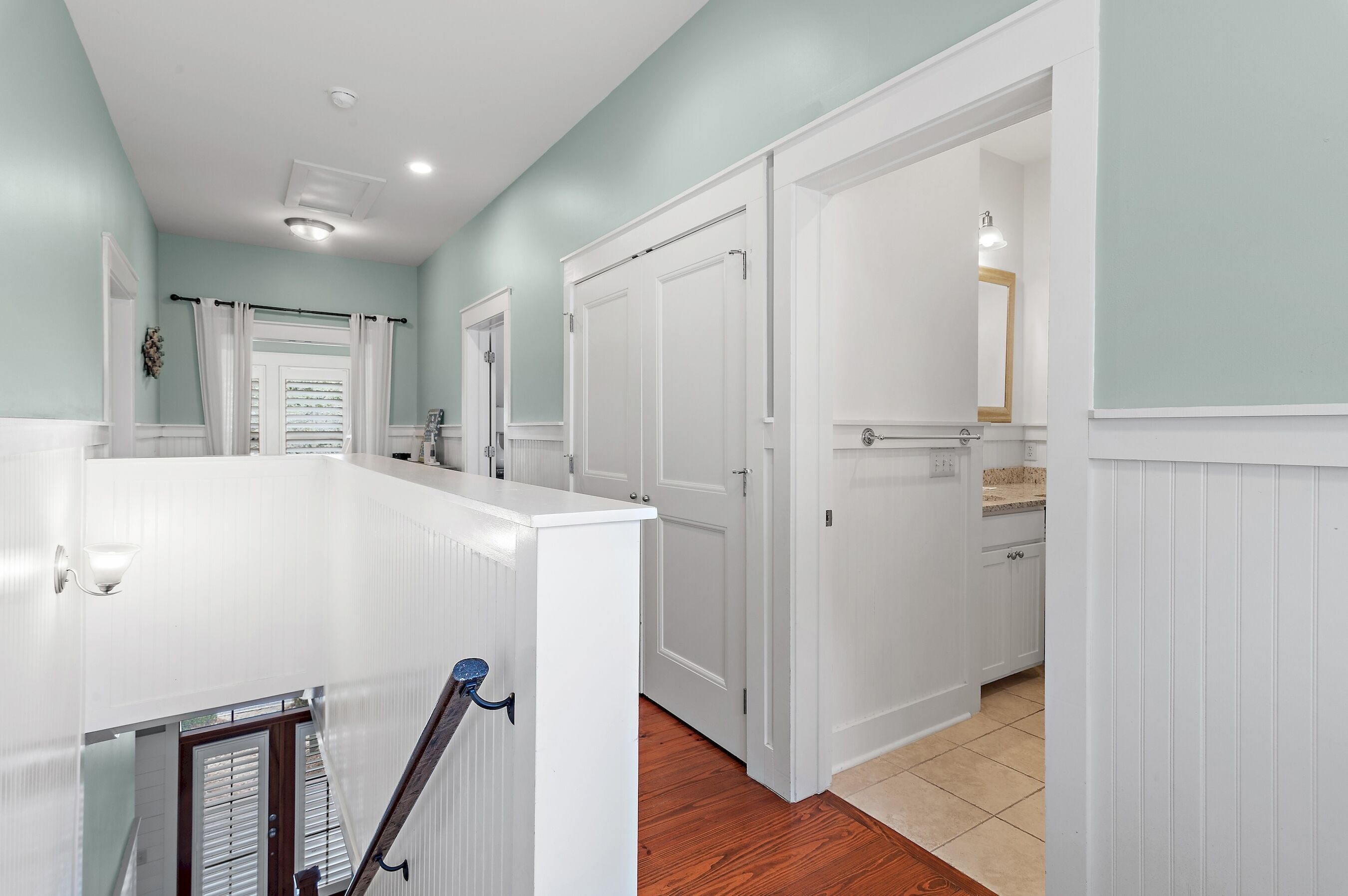 A hallway with white doors, a wooden floor, and a light green wall.