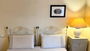 Ein Bett mit gestreiften Kissen und einer karierten Tagesdecke, ein Nachttisch mit einer Lampe und ein gerahmtes Bild an der Wand.