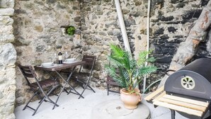 Un mur de pierres avec une table et des chaises, une plante en pot et un barbecue.