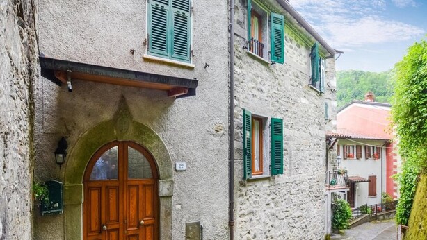Un bâtiment étroit en pierre, doté d’une porte en bois et de volets verts.