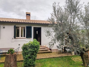 A house with a tiled roof, a chimney, a door, and a small garden with a tree and a bush.