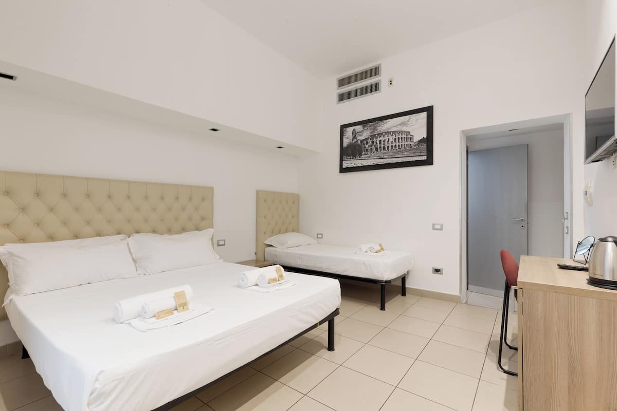 Een hotelkamer met twee bedden, een houten bureau, een stoel, een lijst met een afbeelding aan de muur en een deur.