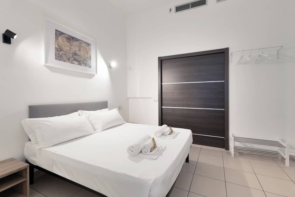 Een moderne hotelkamer met een netjes opgemaakt bed, een groot kunstwerk aan de muur, een donker houten kledingkast en een witte radiator.