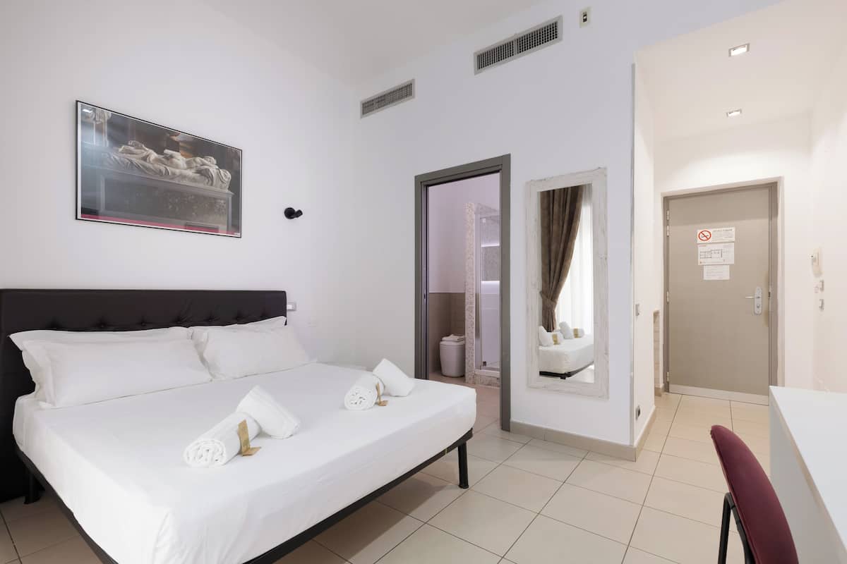 Een hotelkamer met een bed, een schilderij, een deur en een badkamer die door een open deur zichtbaar is.