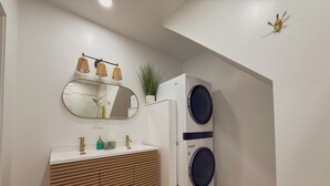 Ein modernes Badezimmer mit einem Holzbadschränken, einem runden Spiegel, einer wandmontierten Leuchte sowie einer integrierten Waschmaschine und einem Trockner.