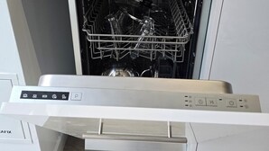 Ett kök med diskmaskin, en skärbräda i trä och en vit diskho.