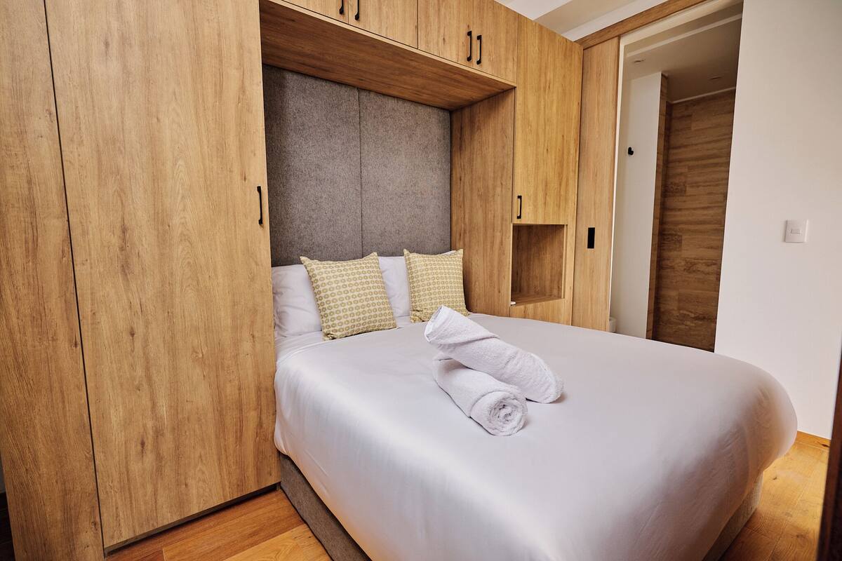 A bedroom with a large bed, wooden wardrobe, and a built-in headboard.