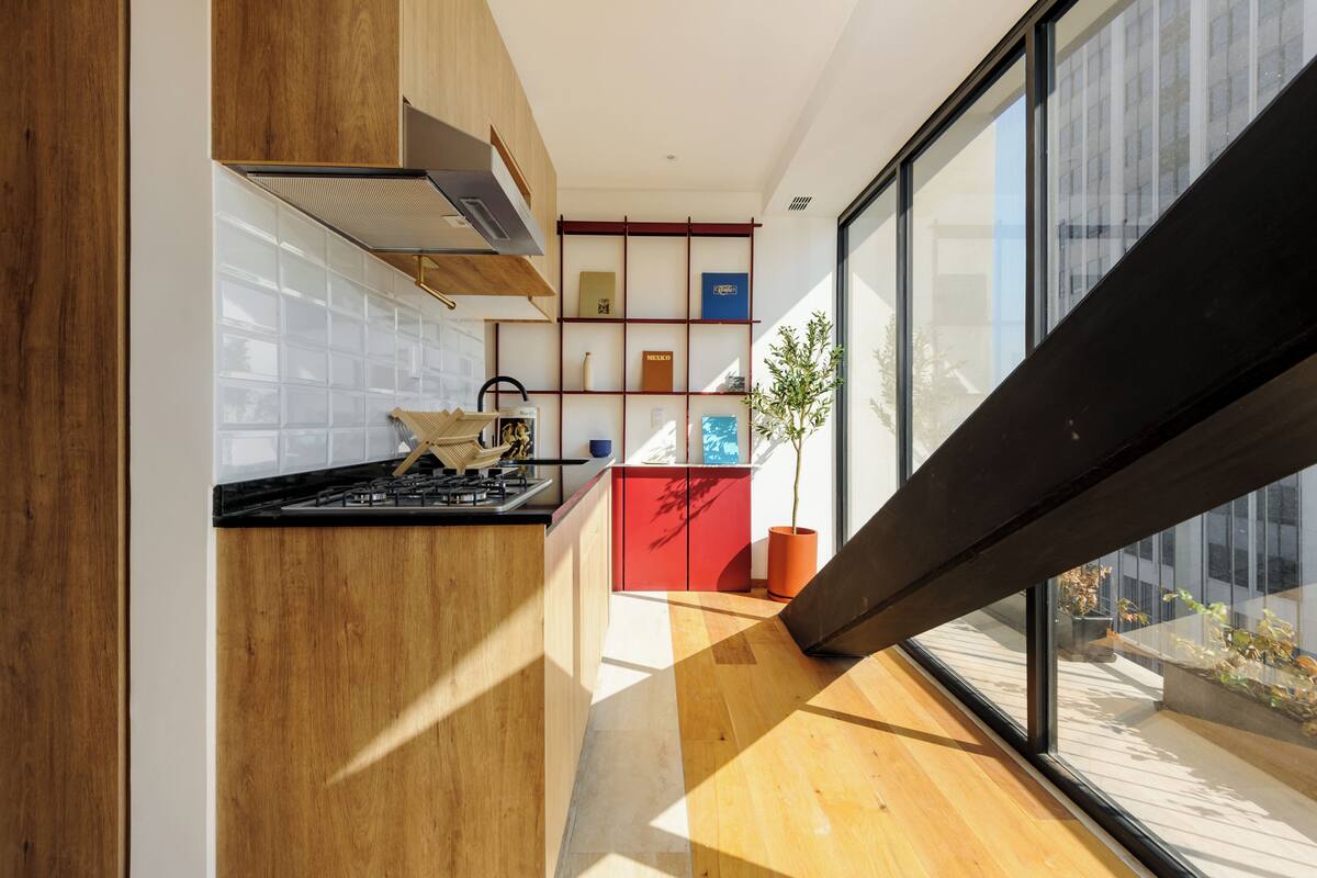 A modern kitchen with wooden cabinets, a gas stove, and a red island. There is a large window providing a view of the outside.