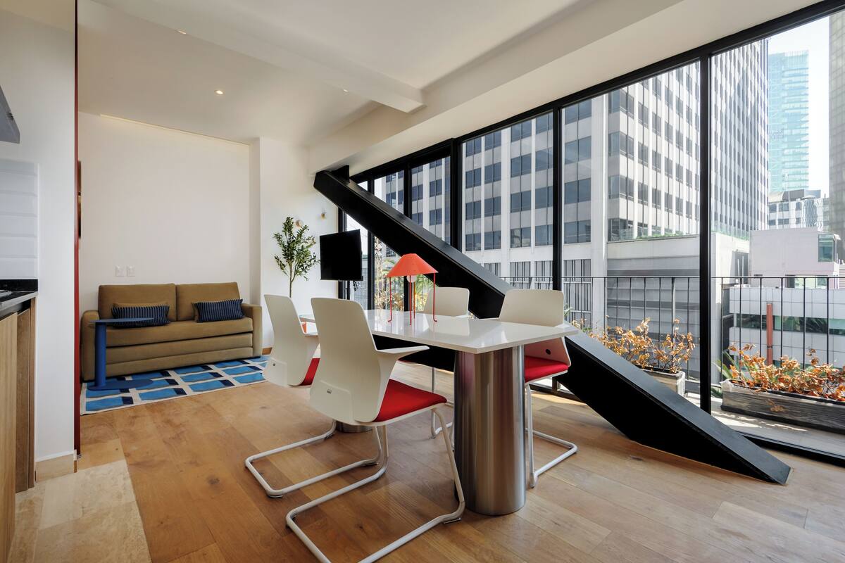 A modern living room with a dining area, large windows, and a view of the city.