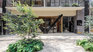 Un edificio moderno con una escalera central, un acceso cubierto y un balcón con plantas.