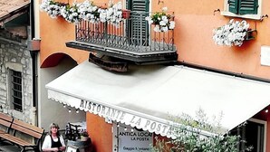 Un área de estar al aire libre con mesas y sillas, un letrero que dice "Ristorante La Posta" y un balcón con flores.