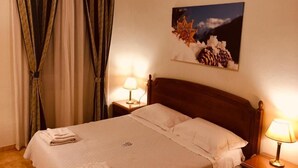Una habitación de hotel con una cama, dos lámparas de noche, un cuadro en la pared y cortinas.
