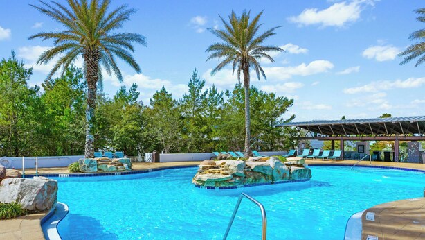 A swimming pool with clear blue water, surrounded by palm trees and lounge chairs.