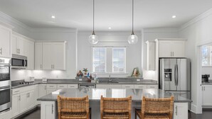 A modern kitchen with white cabinets, a central island with bar stools, stainless steel appliances, and pendant lighting.