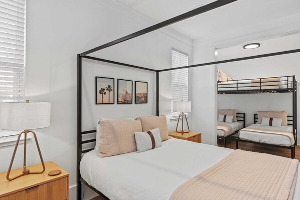 A modern bedroom with a four-poster bed, a bunk bed, and a bedside table with a lamp. - Casa De La Sea by Avantstay Bikes + Golf Cart, Pool Access (Santa Rosa Beach)