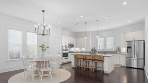 A modern kitchen with white cabinetry, a central island with bar stools, a stainless steel refrigerator, and pendant lighting.