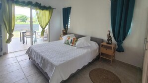 A bedroom with a bed, a nightstand, a chair, and a view of the outdoors.