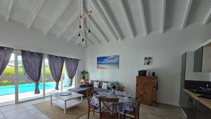 A modern living room with a pool view, a dining area, and a kitchen.