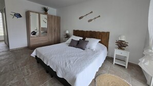 A bedroom with a large bed, a wooden wardrobe, a bedside table with a lamp, and wall-mounted decorations.