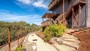 A multi-level wooden structure with outdoor access, surrounded by a fenced garden area with gravel paths and plants. - Charming 3 BD Retreat - Spa, EV Charger, Views (Santa Rosa)