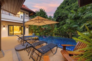 A modern outdoor pool area with lounge chairs and a table, surrounded by lush greenery. - Villa Meraya by Tropiclook   (Rawai)