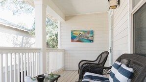 A porch with wicker furniture, a glass table, and a painting on the wall. - 5 Mins to Beach, Shared Pool, Covered Deck, Bikes Heron Cottage by Avantstay (Santa Rosa Beach)