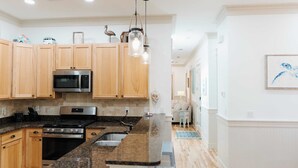 A modern kitchen with wooden cabinets, stainless steel appliances, granite countertops, and pendant lighting. - 5 Mins to Beach, Shared Pool, Covered Deck, Bikes Heron Cottage by Avantstay (Santa Rosa Beach)