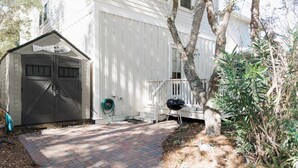 A white building with a garage, a covered porch, and a barbecue grill. - 5 Mins to Beach, Shared Pool, Covered Deck, Bikes Heron Cottage by Avantstay (Santa Rosa Beach)