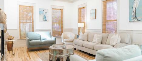 A living room with a ceiling fan, two sofas, a coffee table, and large windows with blinds.