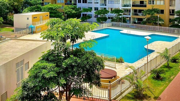 Um edifício de apartamentos alto, com várias varandas, piscina e áreas verdes ao redor.