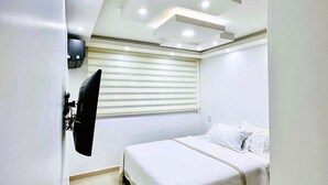 Quarto com cama, televisão na parede e janela com persianas.