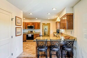 A kitchen with wooden cabinets, granite countertops, and a central island with bar stools.
