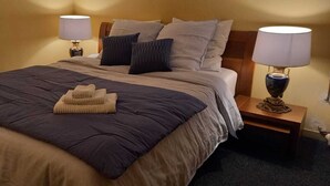 A neatly made bed with a dark blue comforter and beige throw, flanked by two bedside lamps on wooden nightstands.