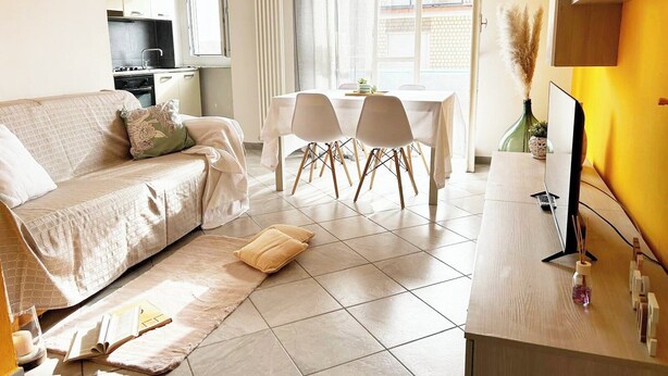 Ein modernes Wohnzimmer mit Sofa, Esstisch mit Stühlen, Küchenzeile und Fernseher auf einem Holzboden.