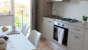 A modern kitchen with a gas stove, oven, and sink. There is a dining table with chairs and a view of the outside through a window. - Quick Home Mimosa - One Bedroom Apartment, Sleeps 4 (Alice Castello)