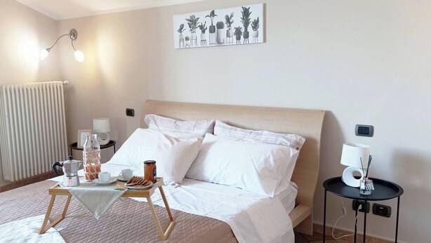 A neatly arranged bedroom with a bed, bedside tables, a radiator, and a wall-mounted artwork. - Quick Home Mimosa - One Bedroom Apartment, Sleeps 4 (Alice Castello)