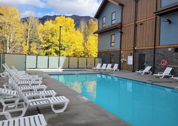 A swimming pool with white lounge chairs and a wooden building with stone accents.