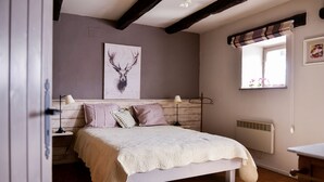 A bedroom with a bed, a window with curtains, a wall-mounted heater, and a painting of a deer. - Le Point du Jour, a charming house (SAPOGNE SUR MARCHE)