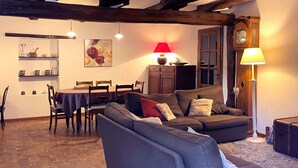 A cozy living room with a sofa, a dining table, and chairs. There is a lamp, a clock, and a painting on the wall. - Le Point du Jour, a charming house (SAPOGNE SUR MARCHE)